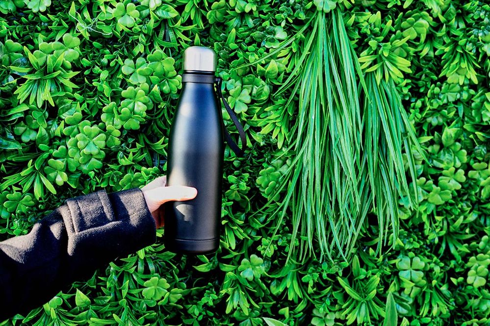 Person holding insulated water bottle in front of greenery. .jpg