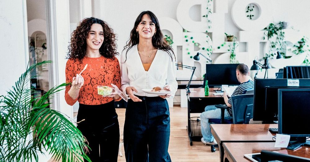 Two smiling female colleagues walk through the office with their lunch.jpg