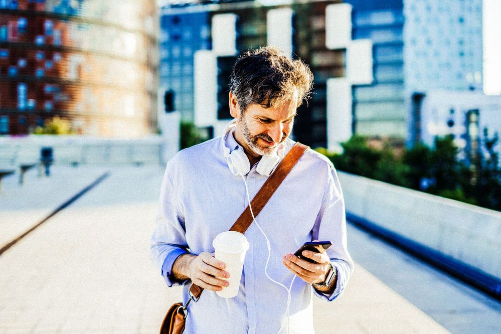 Mid adult man holding coffee cup looking at mobile phone with headphones around neck (4).jpg