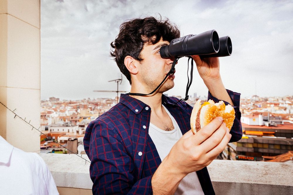 Large_MS PPT_Web-Young man holding a burger, looking across the city through binoculars.jpg