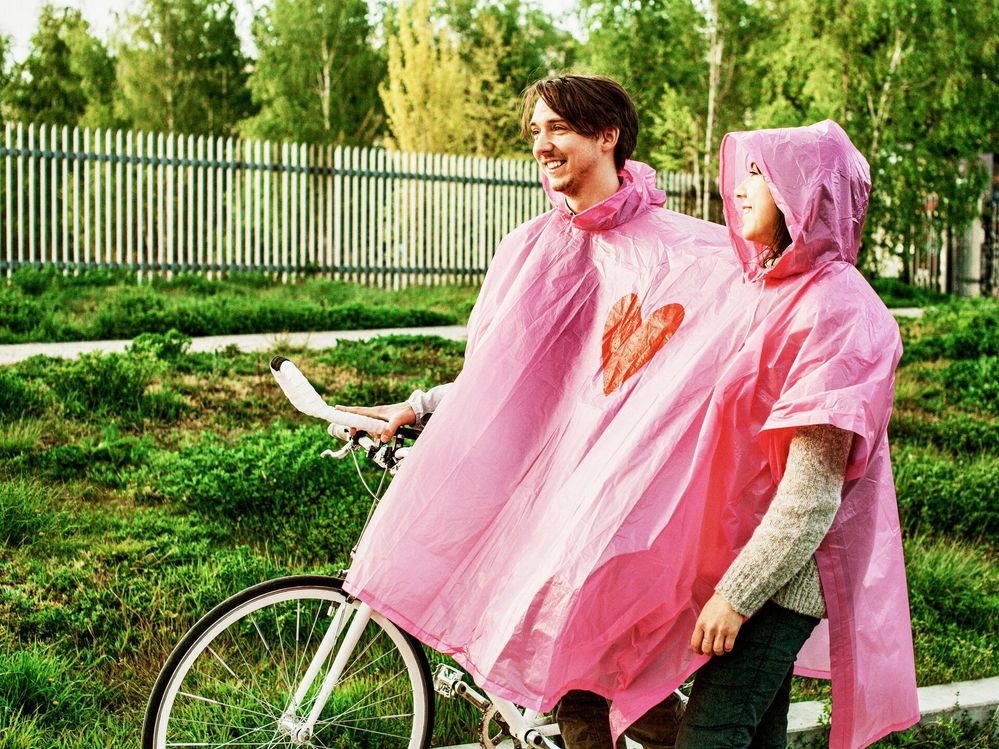 Large_MS PPT_Web-Couple in a two-person poncho with a heart on it, walking with a bicycle on the street. (1).jpg