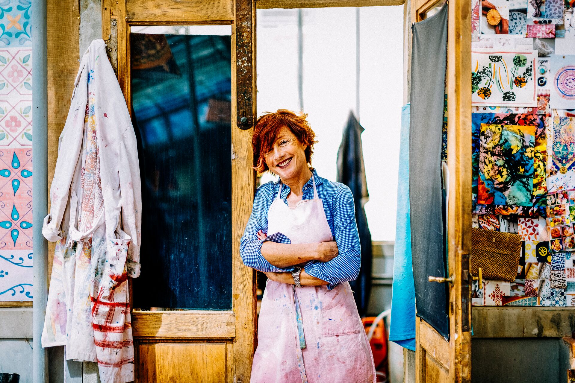 Large_MS PPT_Web-A cheerful woman with red hair in an apron smiles at the camera and rests against the door in her art studio.jpg
