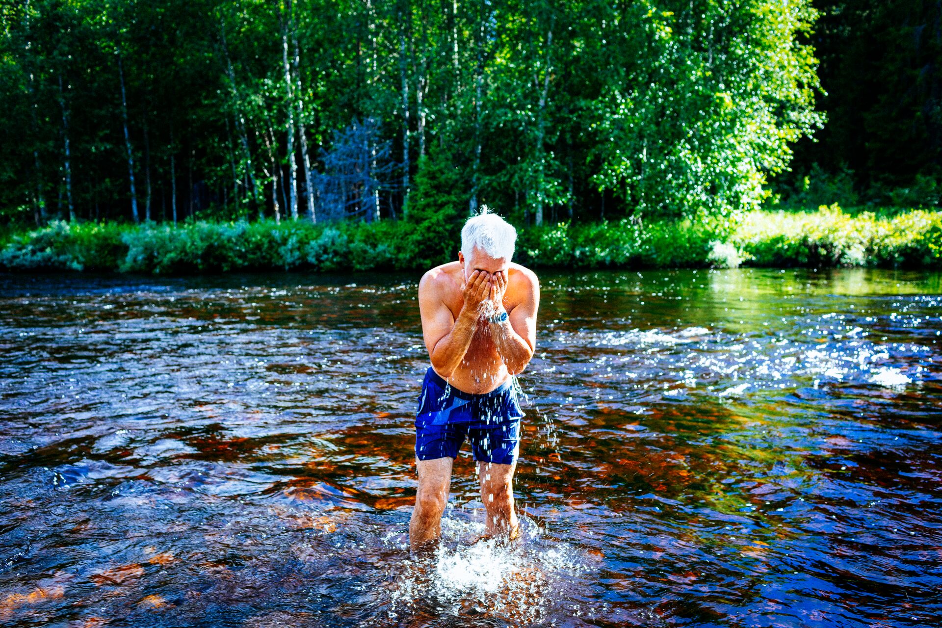 Large_MS PPT_Web-A senior man stands in a river splashing water in his face.jpg
