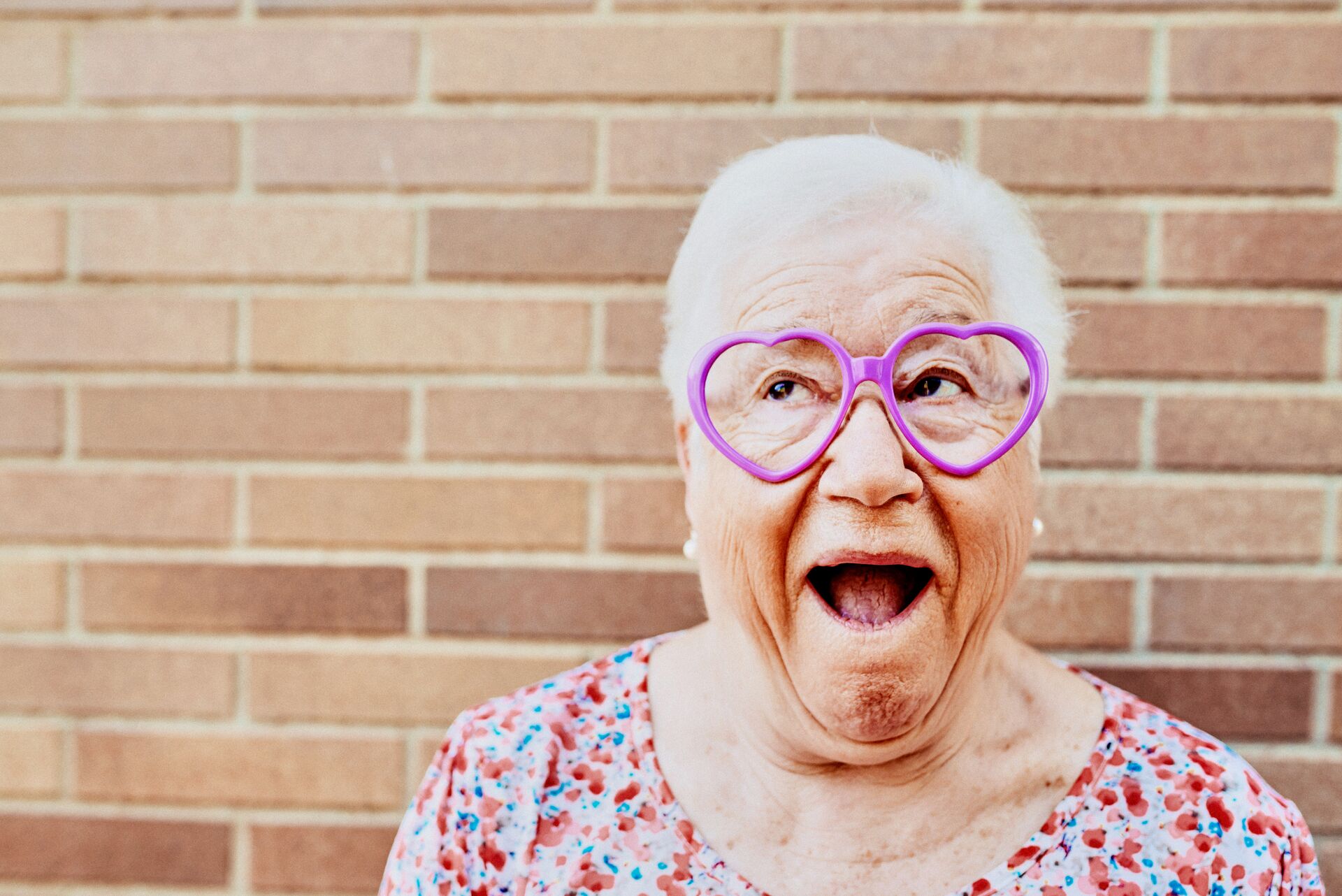 Large_MS PPT_Web-A senior woman with heart-shaped glasses makes a funny face outside in front of a brick wall.jpg