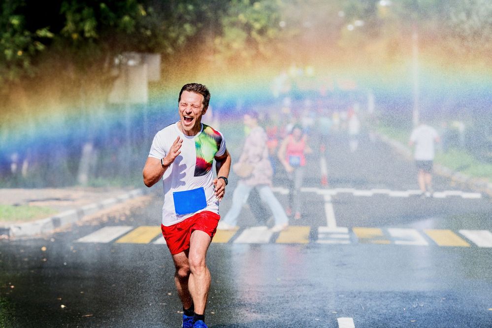 Large_MS PPT_Web-A happy young man screams as he runs a marathon in the rain, causing a rainbow to form behind him.jpg