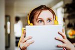 Large_Web and Screen-Young child wearing headphones peeks over her tablet with wide eyes.jpg