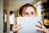 Large_Web and Screen-Young child wearing headphones peeks over her tablet with wide eyes.jpg